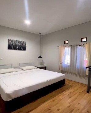Ein Schlafzimmer mit einem großen Bett, einem Nachttisch, einer Pendelleuchte und einem Fenster mit Vorhängen.