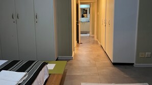 Un corridoio con un letto, una panca e un bagno visibile in lontananza.