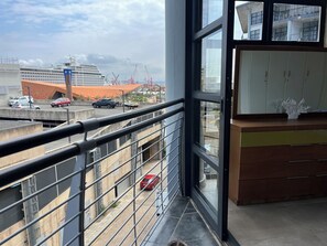 Ein Balkon mit Blick auf ein Kreuzfahrtschiff, geparkte Autos und Baukräne.