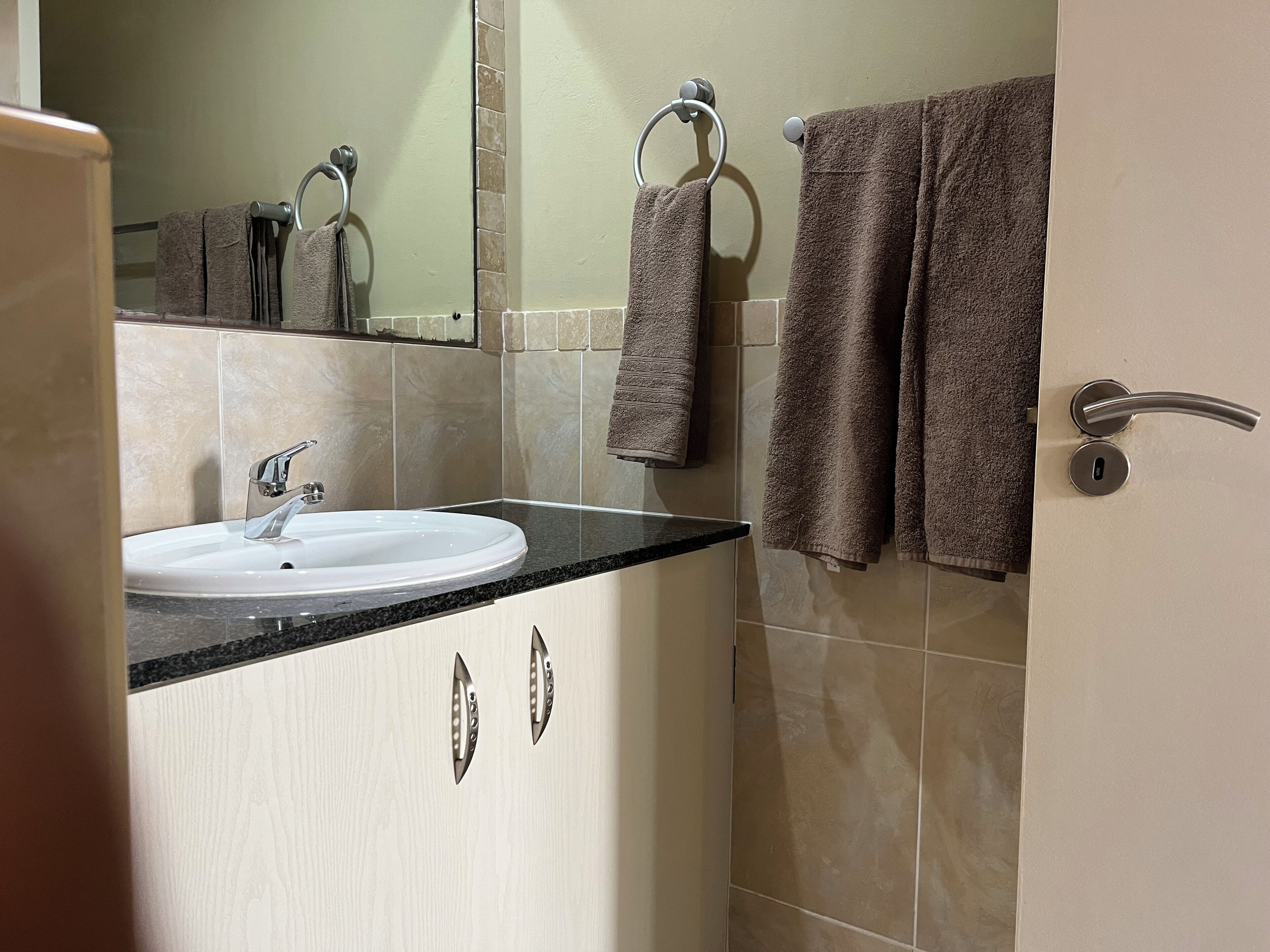 Un baño con lavamanos, aros para toallas y una puerta con picaporte.