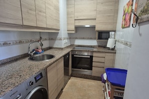 A compact kitchen with a built-in washer, a microwave, and a stainless steel oven. - 45A01 Apartment in Puerto de Vega (Puerto de Vega)