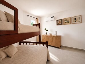 Ein Zimmer mit einem Etagenbett, einem Holztisch und einer Wand-Klimaanlage.