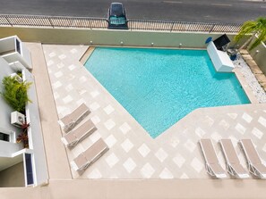 Ein Pool auf dem Dach mit einem geometrischen Muster aus Fliesen, umgeben von Liegestühlen und einer kleinen Gartenanlage.