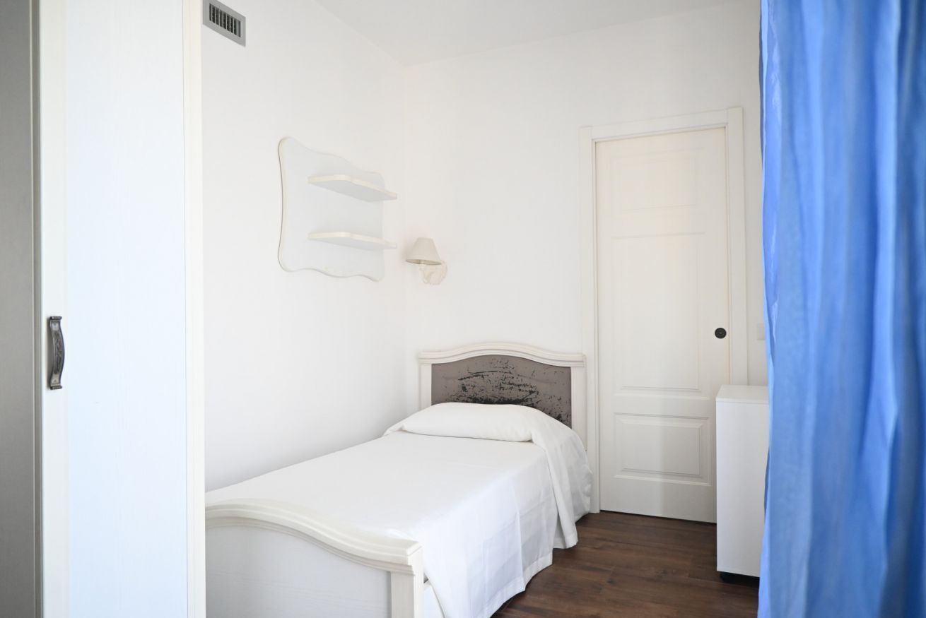 Ein Schlafzimmer mit einem Einzelbett, einer weißen Tür und einem blauen Vorhang.