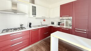 Una cocina moderna con armarios blancos y rojos, electrodomésticos de acero inoxidable y piso de madera.
