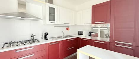 Una cocina moderna con armarios blancos y rojos, electrodomésticos de acero inoxidable y piso de madera.