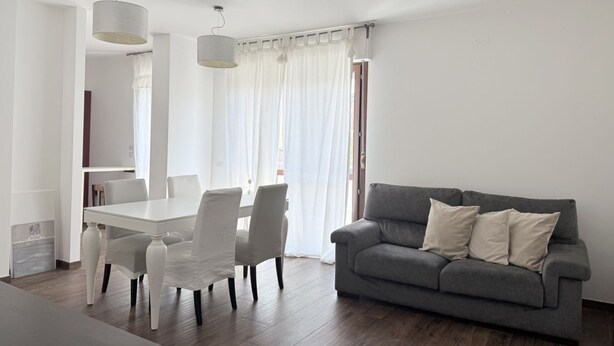 Una sala de estar moderna con una mesa de comedor, sillas, un sofá gris y un ventanal con cortinas.