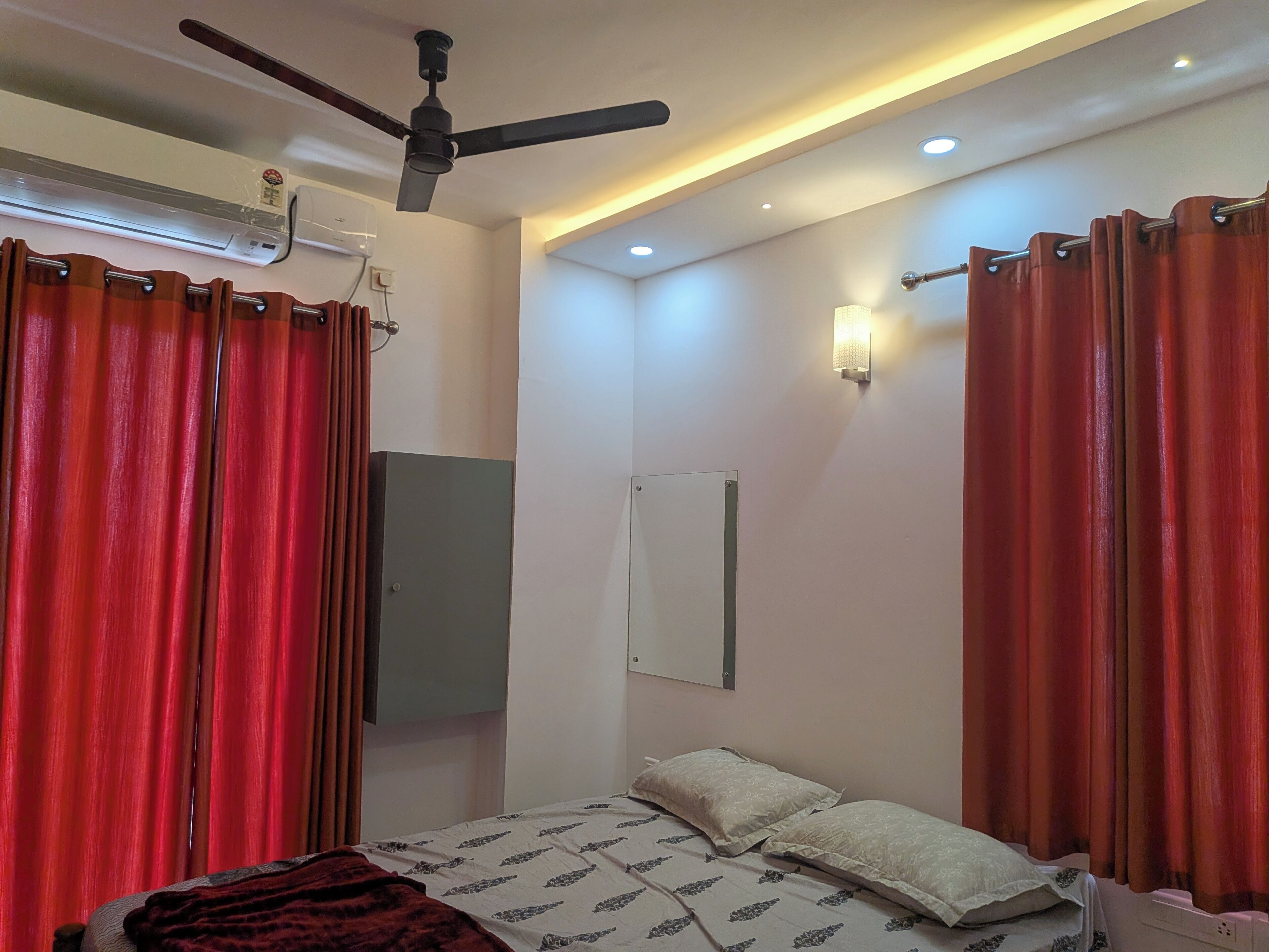 Ein Schlafzimmer mit einem Bett, Vorhängen, einem Deckenventilator, einer Klimaanlage und einer Wandleuchte.