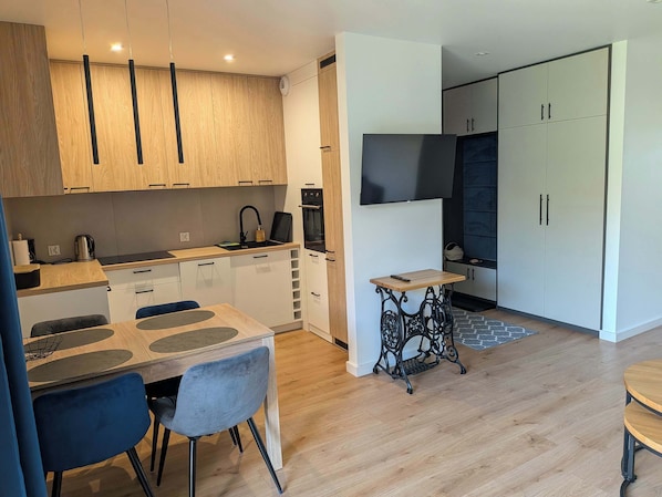 A modern kitchen with wooden cabinets, a dining area with a table and chairs, and a small side table.