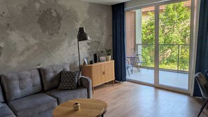 A living room with a sofa, a round wooden coffee table, and a view of a balcony with outdoor furniture. - Klonova Apartment in Masuria (Olecko)