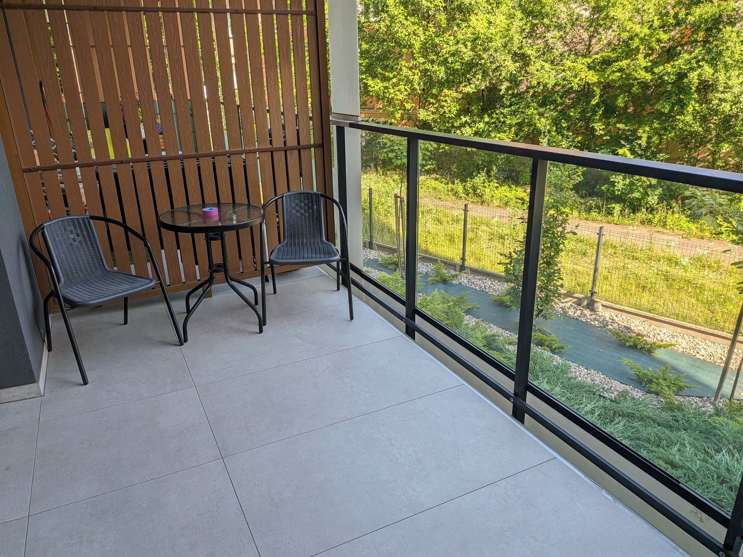 A balcony with two chairs and a small table, overlooking a garden with a water feature.