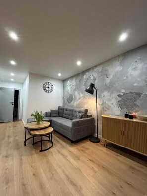 Una sala de estar moderna con un sofá gris, una mesa de centro redonda de madera, una lámpara de pie y un armario.