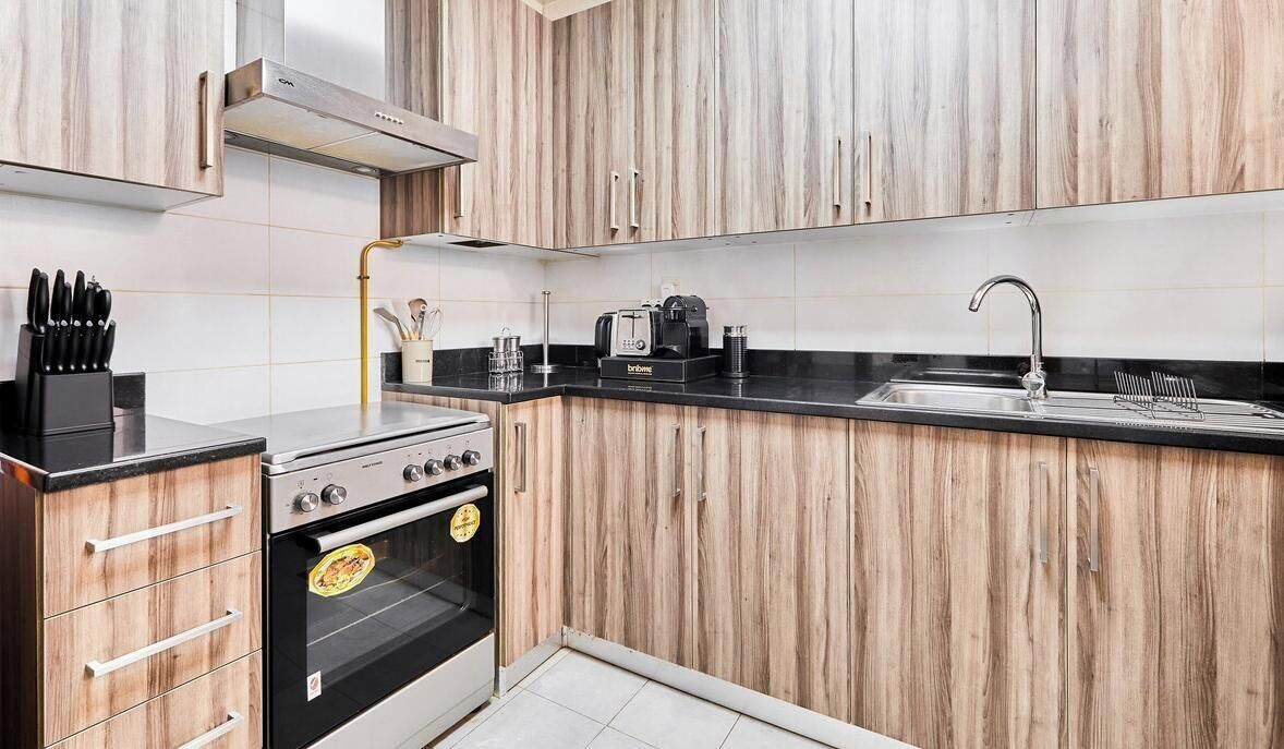 Una cocina moderna con armarios de madera, encimera negra, electrodomésticos de acero inoxidable y horno empotrado.