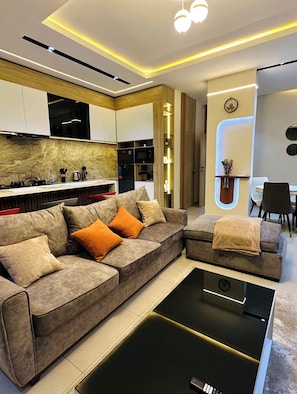Ein modernes Wohnzimmer mit Ecksofa, Couchtisch und integrierten Küchengeräten.