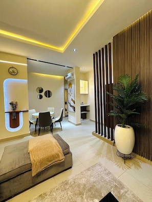 A modern interior with a sofa, dining area, and a large potted plant. - Lushplus Living Shortlet (Abuja)