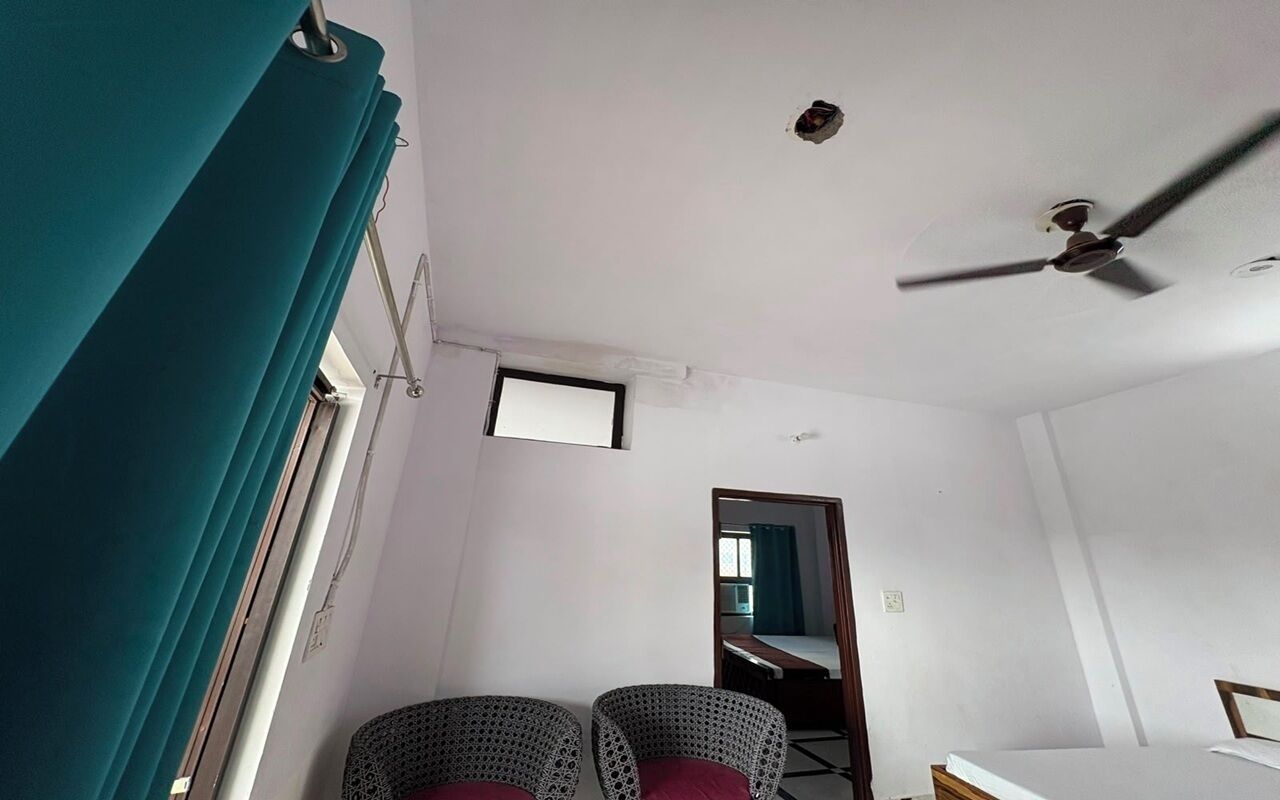 A room with a ceiling fan, a bed, two chairs, and a window with curtains.
