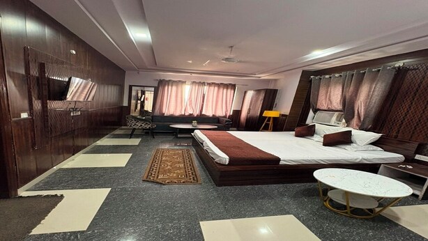 A hotel room with a bed, a round table, a sofa, a desk, and a chair. - Gayatri Seva Dham (Vrindavan)