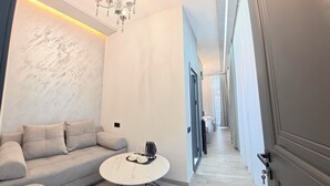 Una habitación de hotel moderna con piso de mármol, un sofá, una pequeña mesa redonda con una cafetera y un candelabro.