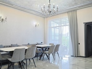 Una sala da pranzo con un tavolo rotondo, sedie rivestite di grigio, un lampadario e un'ampia finestra con tende.
