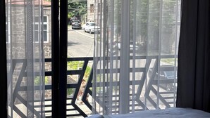 Habitación de hotel con cama, ventana con vista a la calle y balcón con barandilla.