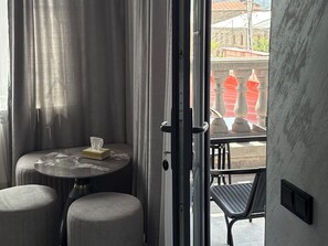 A room with a small round table, two cushioned chairs, a tissue box, and a door leading to an outdoor area with a railing and a view of buildings. - Leader Hotel (Goris)