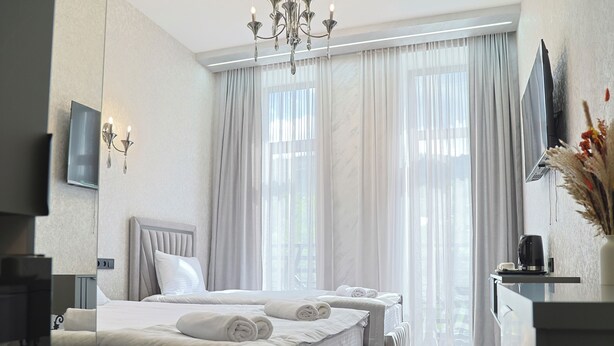 Una habitación de hotel con cama, mesitas de noche, televisor y un ventanal con cortinas.