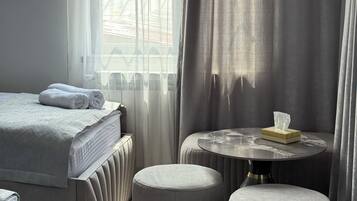 Una habitación de hotel con una cama, una mesa redonda y una caja de pañuelos, junto con dos otomanas.
