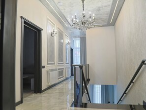 A hallway with a marble floor, a chandelier, and a staircase with a metal railing. - Leader Hotel (Goris)