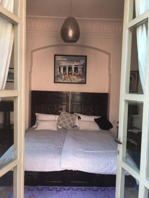 Ein Bett mit gemustertem Überwurf, einem Kopfteil mit dekorativen Schnitzereien und einem Bild darüber.