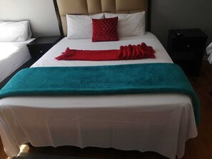 Un lit recouvert d’une courtepointe blanche, d’une couverture turquoise et agrémenté d’un coussin rouge.