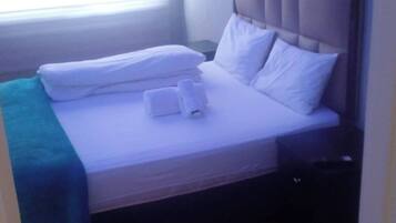 A hotel room with a bed, pillows, a blanket, and a nightstand.