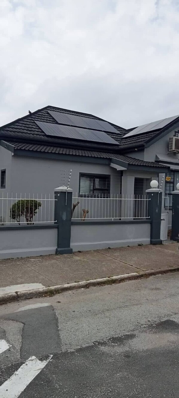 A residential building with a grey facade, a tiled roof, and a gated entrance.