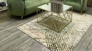 Un salón con un sofá verde, un sillón a juego, una mesa de centro de vidrio y una alfombra estampada.