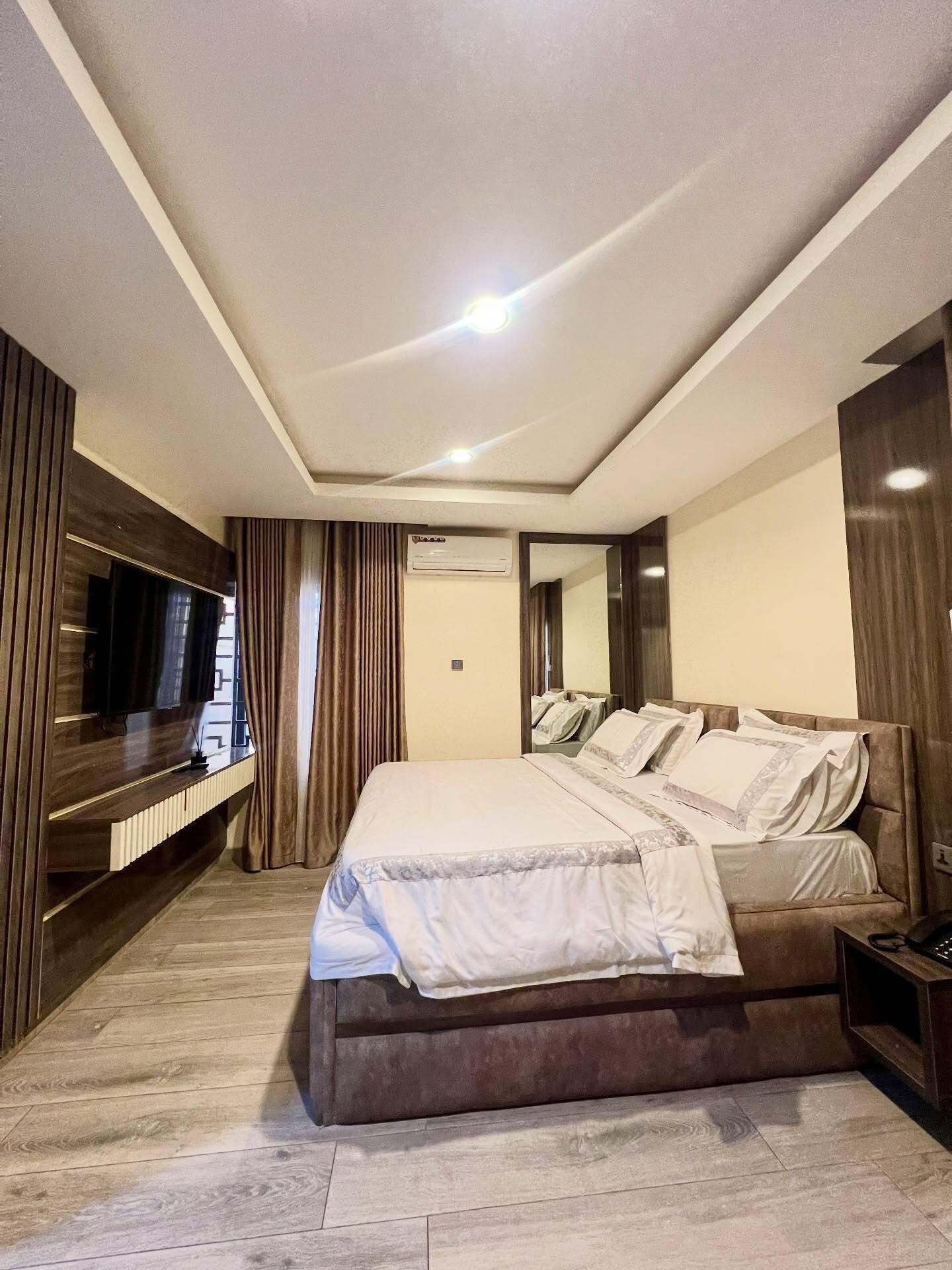 Habitación de hotel moderna con una cama grande, televisión de pantalla plana, aire acondicionado integrado y suelo de madera.