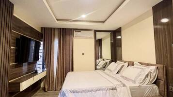 Habitación de hotel moderna con una cama grande, televisión de pantalla plana, aire acondicionado integrado y suelo de madera.