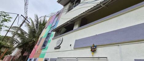 A multi-story building with a colorful facade, a gated entrance, and a contact number displayed.