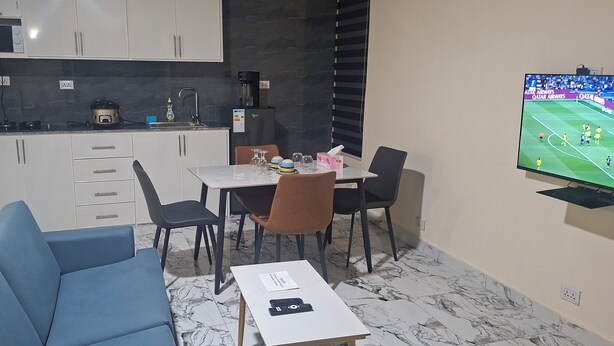 A compact living space with a kitchenette, a dining area, and a TV displaying a sports event.