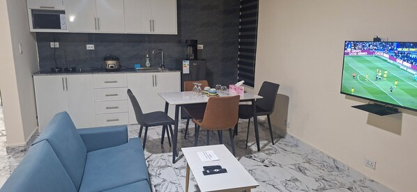 A compact living space with a kitchenette, a dining area, and a TV displaying a sports event.