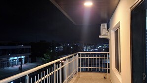 Un balcon avec une rambarde en métal, une fenêtre et une vue sur le paysage urbain illuminé la nuit.