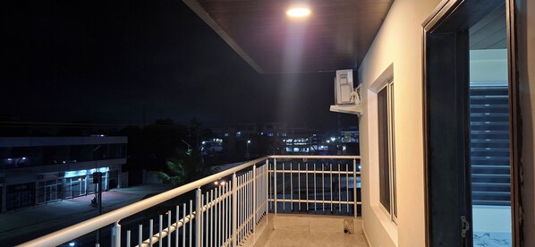 A balcony with a metal railing, a window, and a view of a cityscape at night. - TEE GUEST HOUSE (Monrovia)