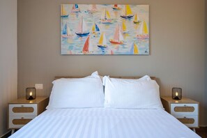 Ein Hotelzimmer mit einem Bett, zwei Nachttischen und einem Bild von Segelbooten an der Wand.