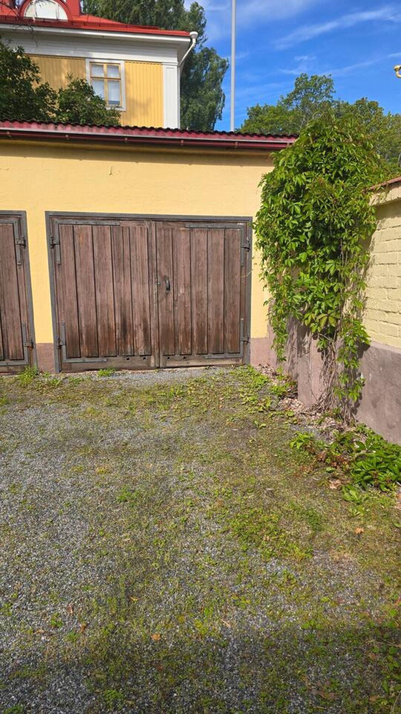 A building with two large wooden doors, a gravel driveway, and a wall with climbing plants.