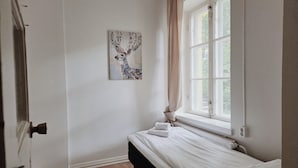 Ein Schlafzimmer mit einem Bett, einem Fenster mit Vorhängen, einer Heizung und einem an der Wand hängenden Kunstwerk.