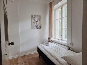 Ein Schlafzimmer mit einem Bett, einem Fenster mit Vorhängen, einer Heizung und einem an der Wand hängenden Kunstwerk.