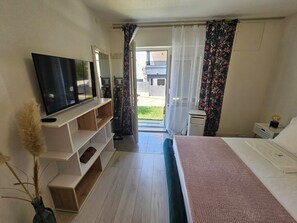 Ein Hotelzimmer mit Bett, Fernseher, Schreibtisch und einem fensterbelaubten Fenster.