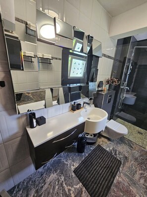 Ein modernes Badezimmer mit Marmorplatte, Waschbecken in Weiß, einem Spiegel und einer Duschkabine.