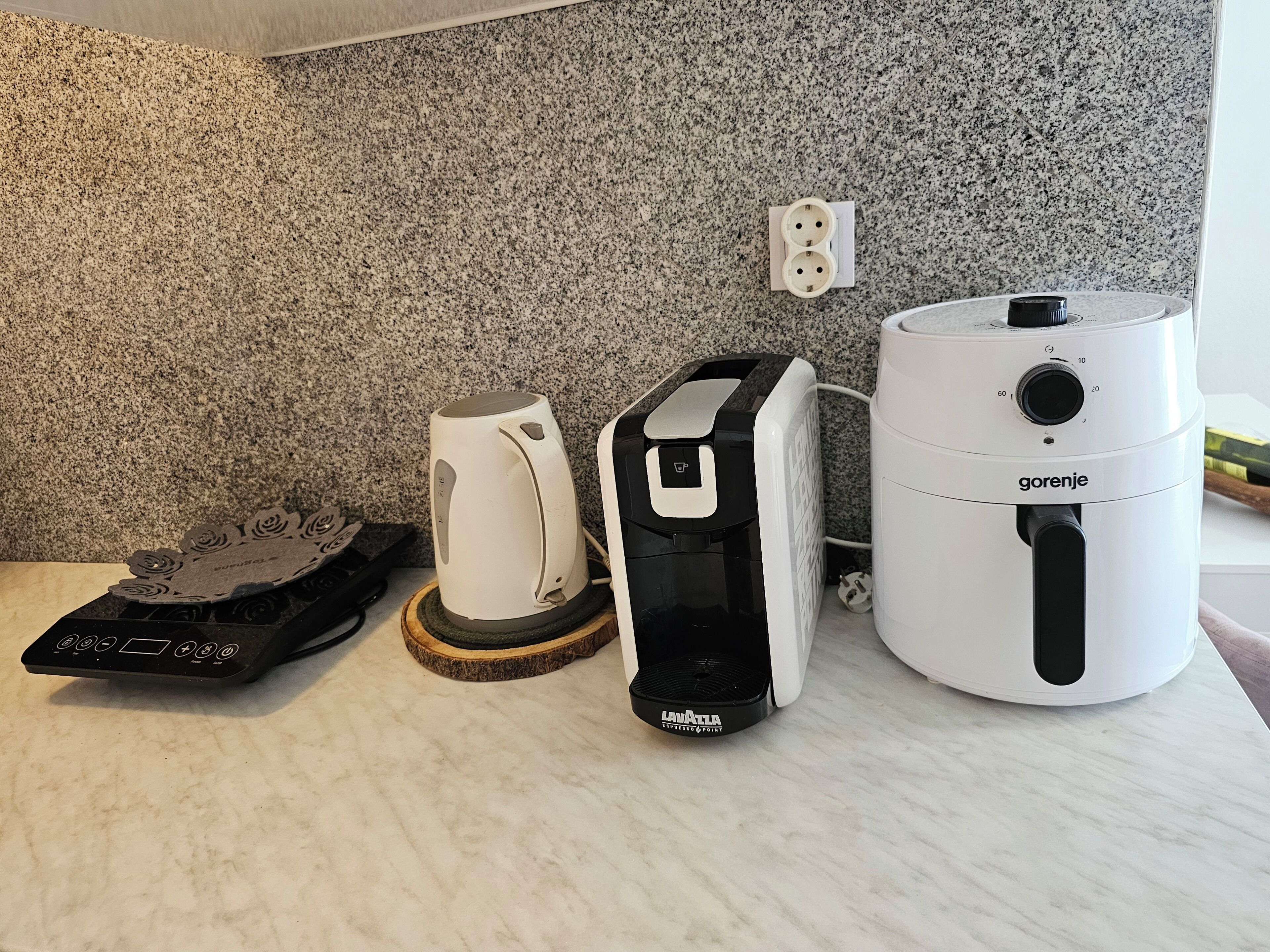 A kitchen with a granite countertop, a coffee maker, a kettle, and a white appliance with the brand 'gorenje'.