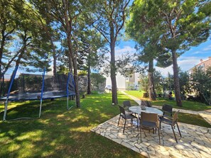 Ein Garten mit Trampolin, einer Steinterrasse und Gartenmöbeln sowie einem Rasen.