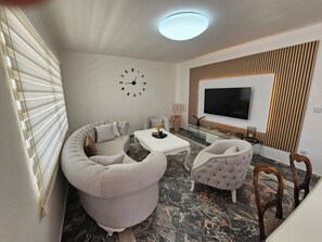 Ett modernt vardagsrum med en soffa, fåtöljer, ett soffbord, en tv och en väggklocka.