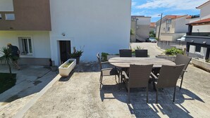 An outdoor patio with a table and chairs, potted plants, and a building entrance. - Casa Carmel (Kamen)